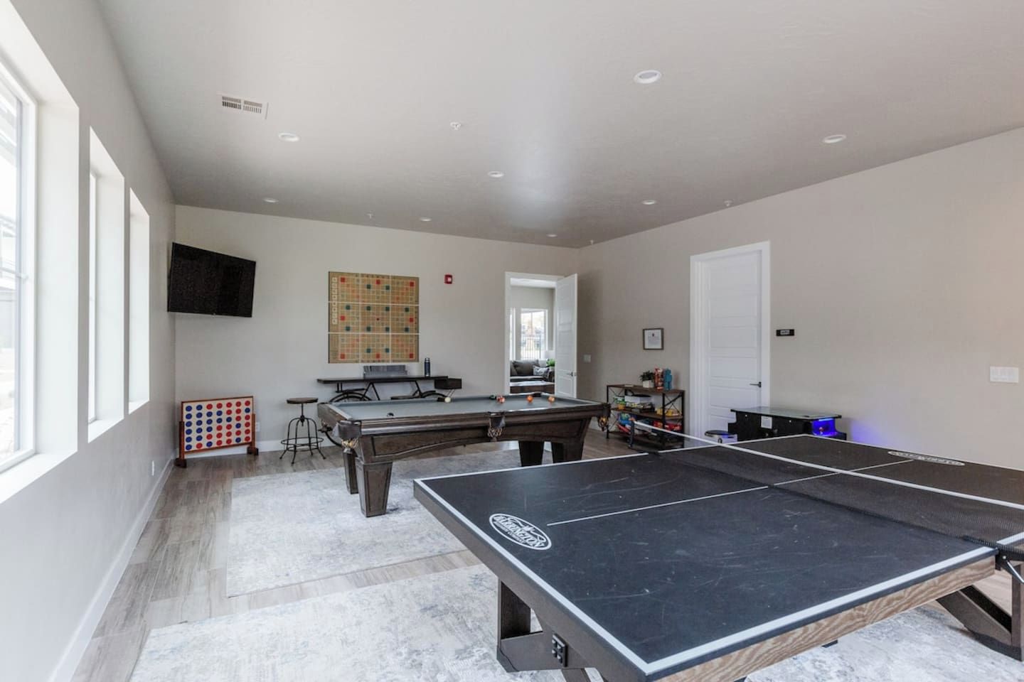 Una habitación amplia con mesa de ping pong, mesa de billar y un ventanal que proporciona luz natural.
