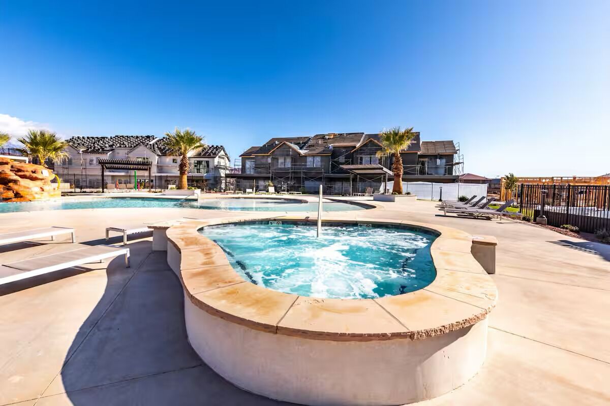 A swimming pool with a hot tub, lounge chairs, and a building with a covered patio in the background.