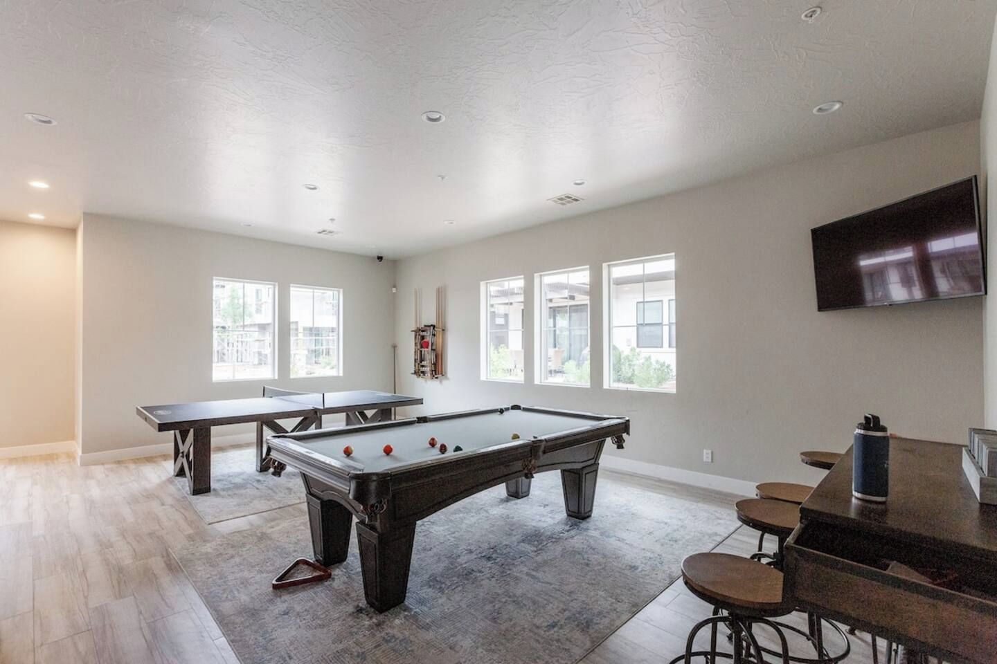 A spacious room with a pool table, a bar area, and large windows providing natural light.