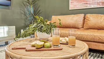 A round wicker table with a potted plant, a cutting board with fruit, and two glasses of juice.