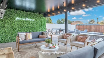 An outdoor patio with a green wall, seating area, and a ceiling with string lights.