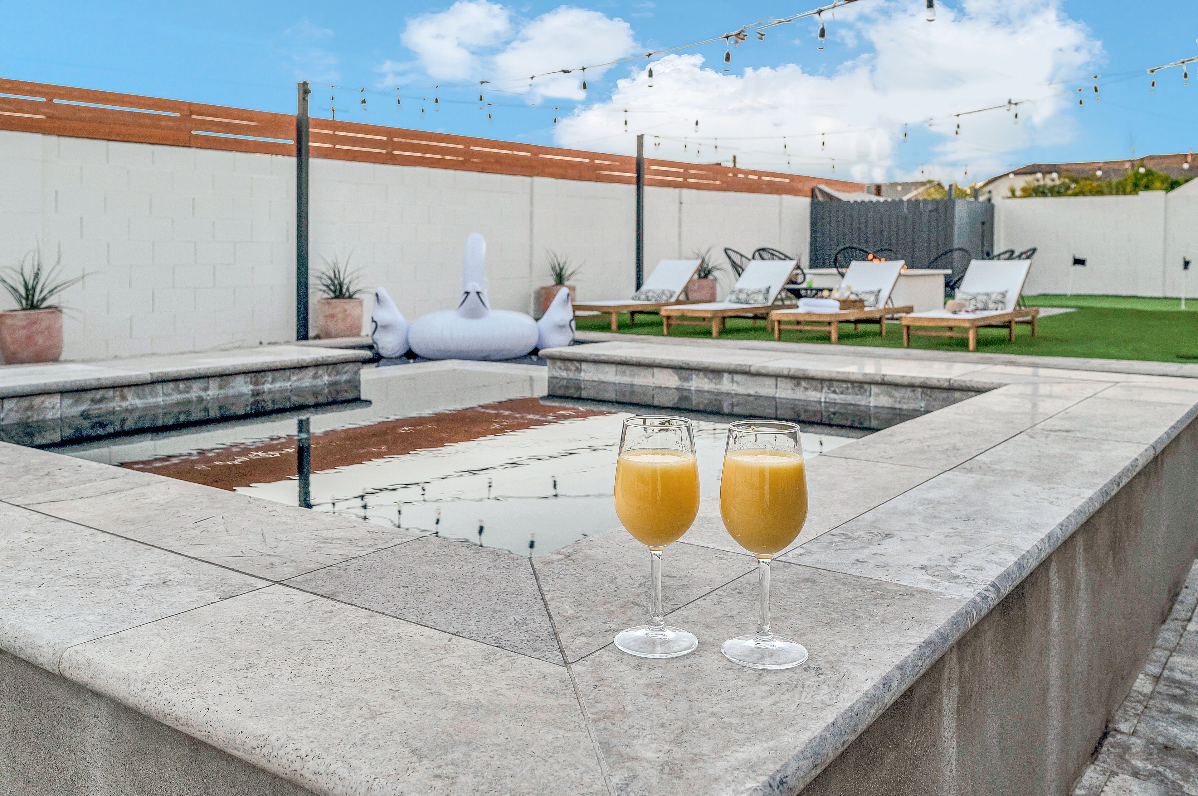 Un espace piscine avec des chaises longues et deux verres de jus d’orange.