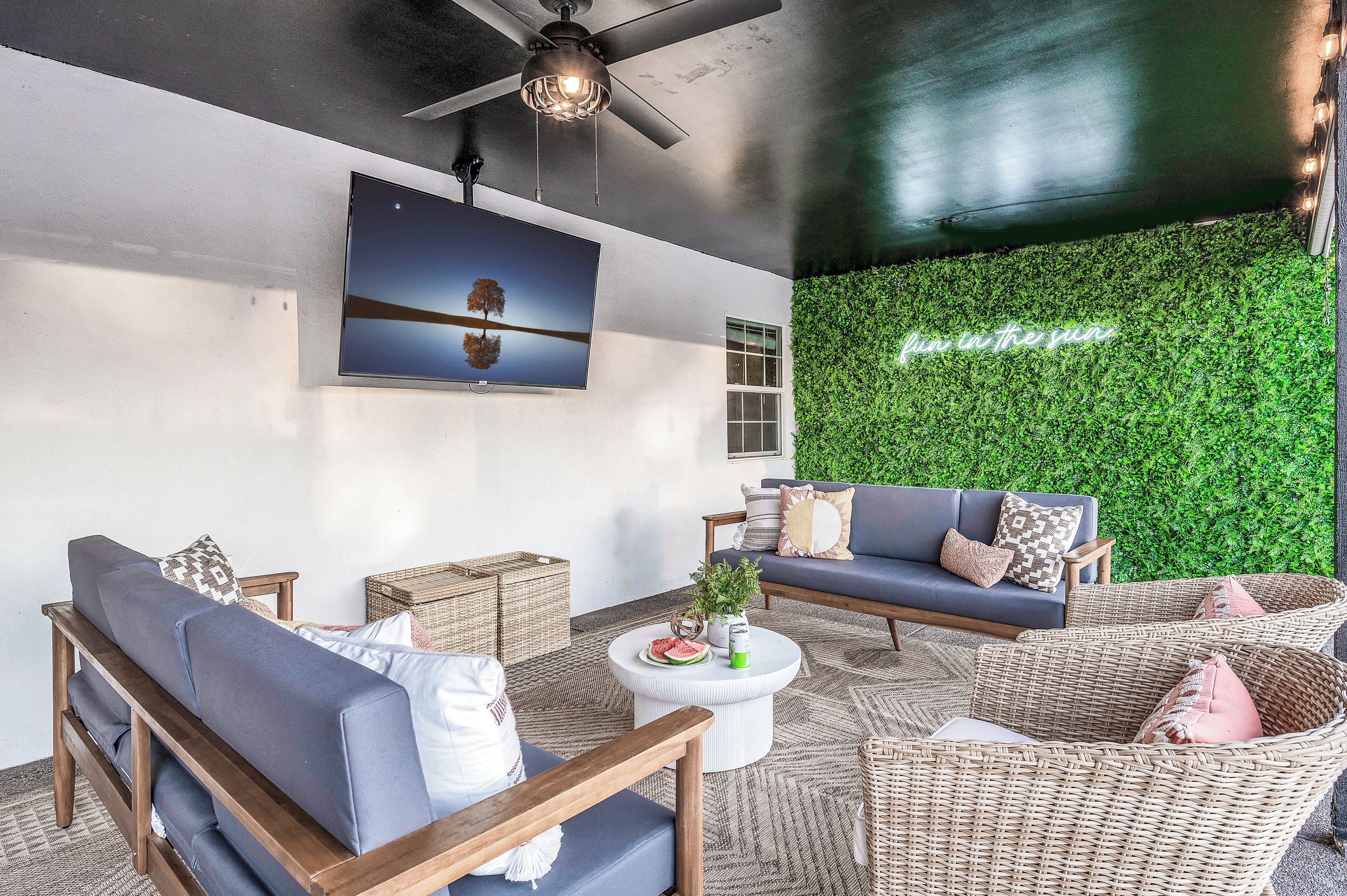 A modern living room with a ceiling fan, a large flat-screen TV, and a green wall with a 'fun in the sun' sign.