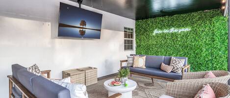 A modern living room with a ceiling fan, a large flat-screen TV, and a green wall with a 'fun in the sun' sign.