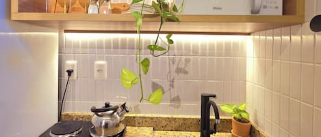 A kitchen with a microwave, a kettle, a sink, and a potted plant.