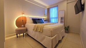 A modern bedroom with a large bed, bedside tables, a flat-screen TV, and a potted plant. - Jardins do Atlântico By Hosppedar (João Pessoa)