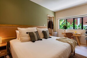 A hotel room with a large bed, a desk, and a window with a view of greenery.