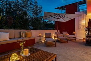 An outdoor seating area with a sofa, lounge chairs, a table, and a large umbrella.