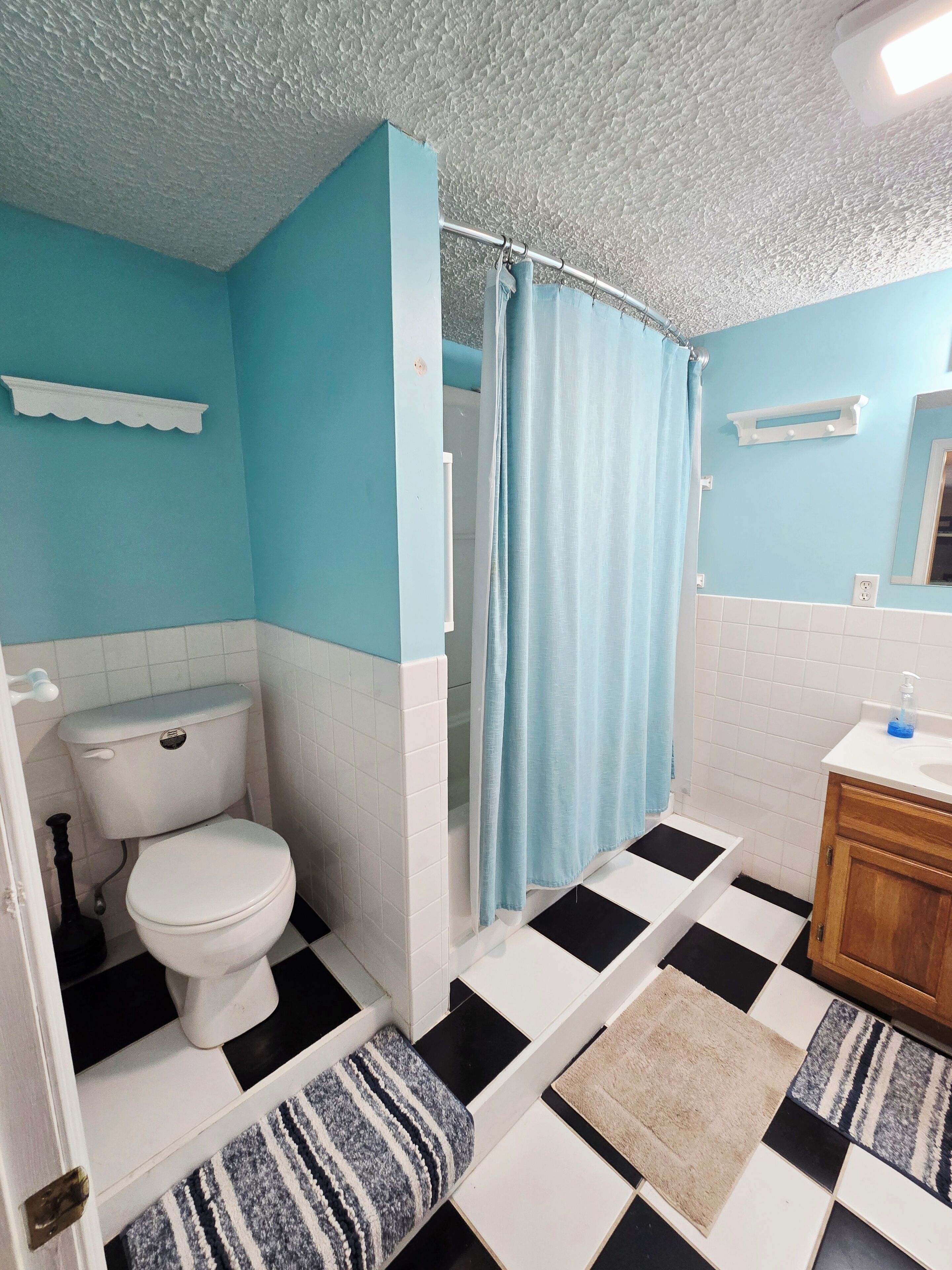 A bathroom with a toilet, a shower curtain, a sink, and a mirror.