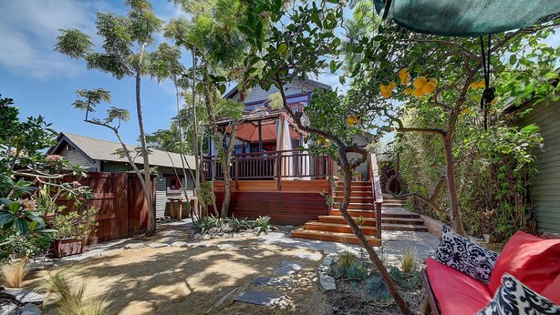 Ein Garten mit einer Holztreppe, die zu einer Veranda führt, umgeben von Pflanzen und einer roten Sitzgelegenheit im Freien.