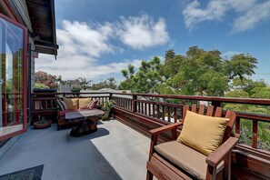 A balcony with wooden furniture, including a bench and a chair, and a view of trees and buildings in the background. - Historic Craftsman - Pet Friendly - Sleeps 6 (Long Beach)