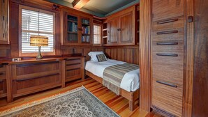 Ein Schlafzimmer mit einem Bett, einem Holzschrank, eingebauten Bücherregalen und einem Schreibtisch mit Lampe.