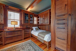 A bedroom with a bed, wooden wardrobe, built-in bookshelves, and a desk with a lamp. - Historic Craftsman - Pet Friendly - Sleeps 6 (Long Beach)