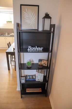 Ein schwarzes Bücherregal mit dem Schriftzug 'Bonheur' in der Mitte, gefüllt mit Büchern, einer kleinen Pflanze und einem Gesellschaftsspiel.