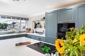 A modern kitchen with a large island, built-in appliances, and a view of the outside. - Vitamin Sea - Swimming Pool, Hot Tub, Sea Views (Saundersfoot)