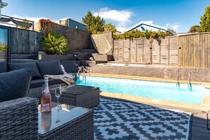 A backyard with a swimming pool, outdoor furniture, and a wooden fence. - Vitamin Sea - Swimming Pool, Hot Tub, Sea Views (Saundersfoot)