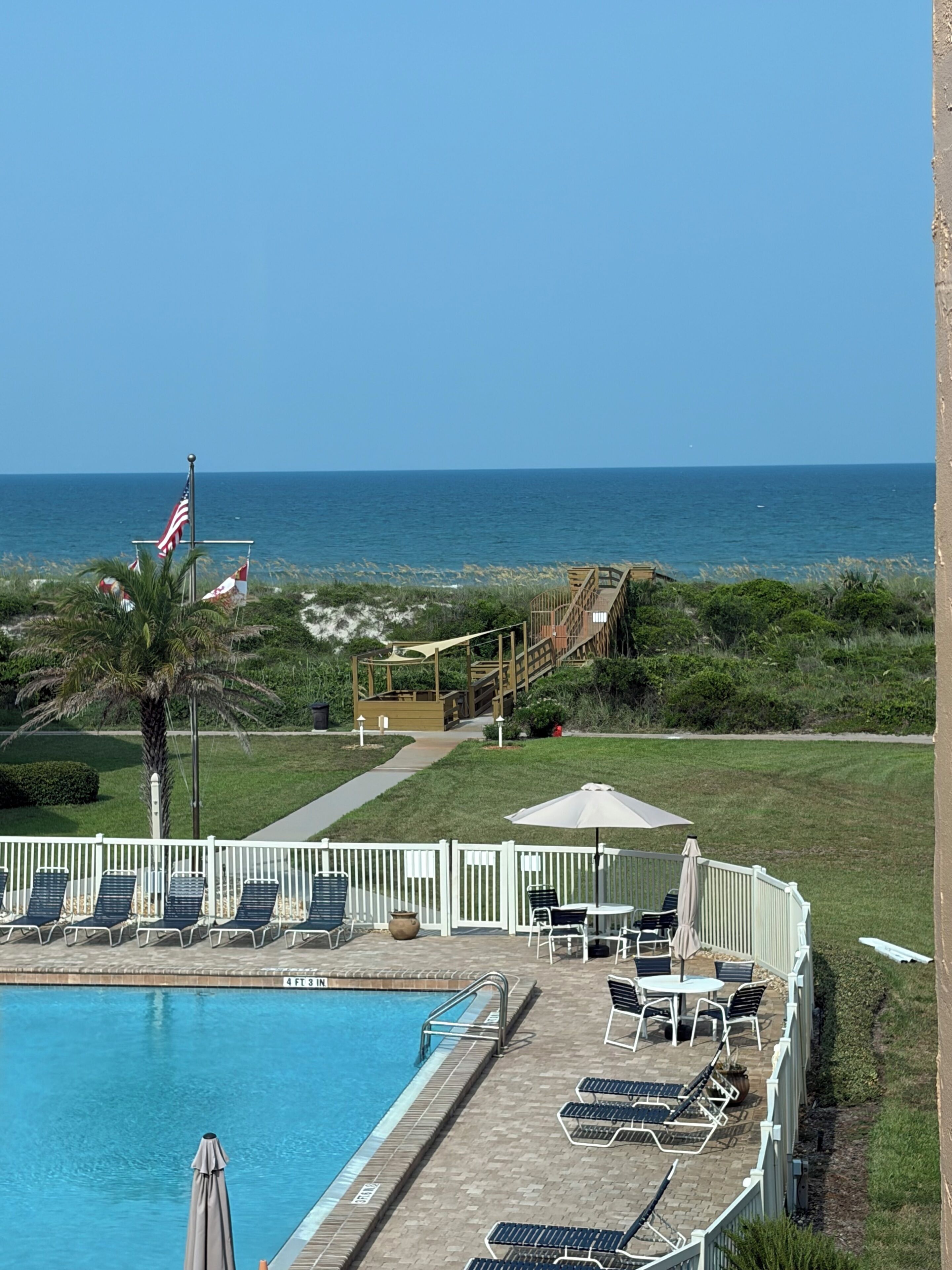A pool area with lounge chairs and umbrellas, a wooden deck, and a view of the ocean.