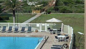 Un espace piscine avec des chaises longues et des parasols, une terrasse en bois et une vue sur l’océan.