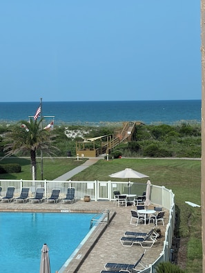 A pool area with lounge chairs and umbrellas, a wooden deck, and a view of the ocean. - Beachfront condo with direct pool & ocean view on Crescent Beach (St. Augustine)