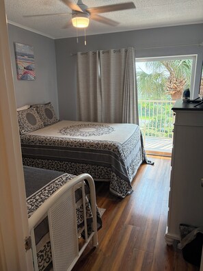 Ein Schlafzimmer mit einem Bett, einem Deckenventilator, einem Fenster mit Vorhängen und Blick auf Grünfläche.
