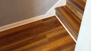 Un escalier en bois avec une rampe, un mur blanc et un interrupteur.