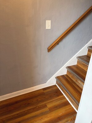 A wooden staircase with a handrail, a white wall, and a light switch. - Beachfront condo with direct pool & ocean view on Crescent Beach (St. Augustine)