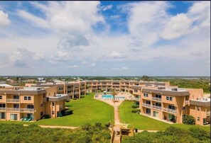 A multi-story hotel with a central courtyard, outdoor pool, and a view of the surrounding landscape. - Beachfront condo with direct pool & ocean view on Crescent Beach (St. Augustine)