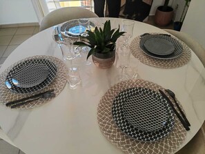 Ein runder Esstisch, gedeckt mit Tellern, Besteck und Gläsern, umgeben von Stühlen.