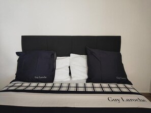 Ein Bett mit schwarzem Kopfteil, zwei Kissen und einer Bettdecke in Weiß und Schwarz mit 'Guy Laroche'-Aufschrift.