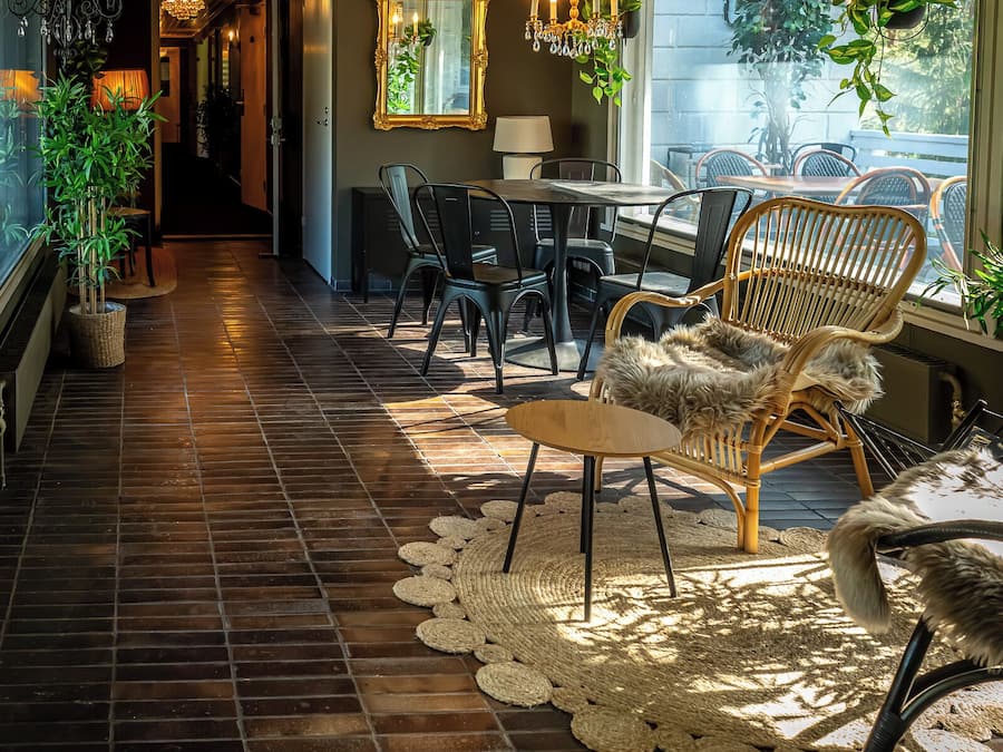 Een hal met een houten vloer, een eethoek met stoelen en een tafel, en een groot raam met planten.