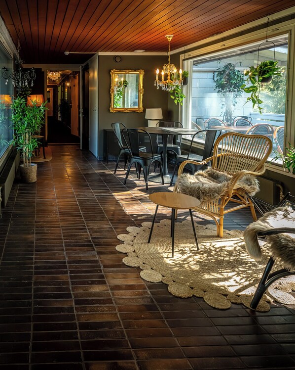A hallway with a wooden floor, a dining area with chairs and a table, and a large window with plants.