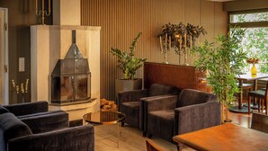 Una sala de estar moderna con chimenea, sillones tapizados oscuros, una mesa de comedor de madera y un ventanal con plantas.