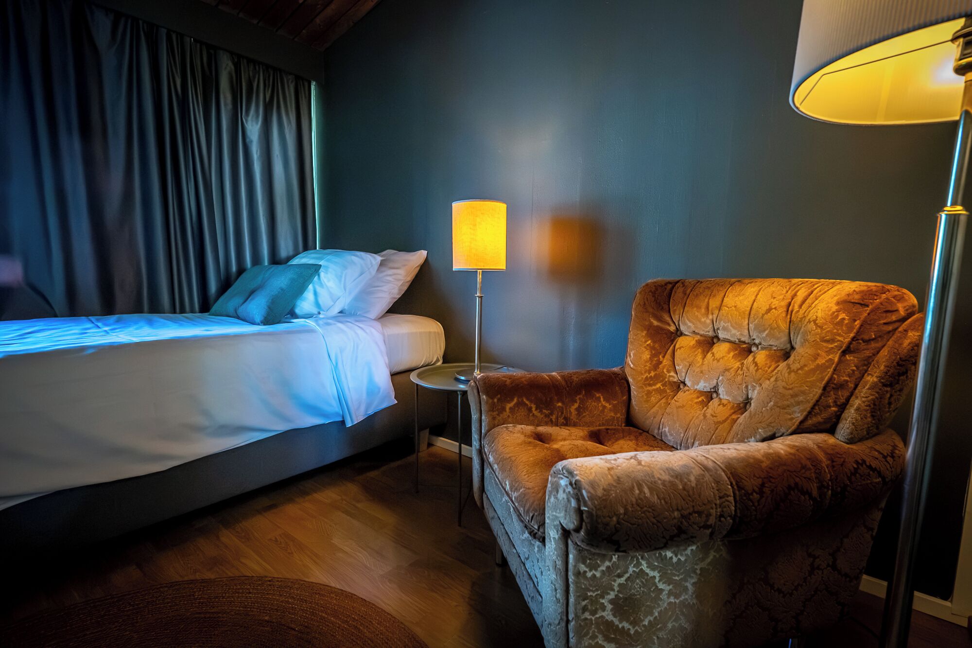 A hotel room with a bed, a chair, a lamp, and a curtain.