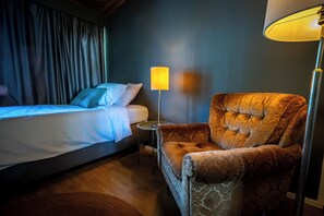 A hotel room with a bed, a chair, a lamp, and a curtain.