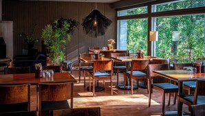 Interior de restaurante con mobiliario de madera, ventanas amplias y plantas de interior.