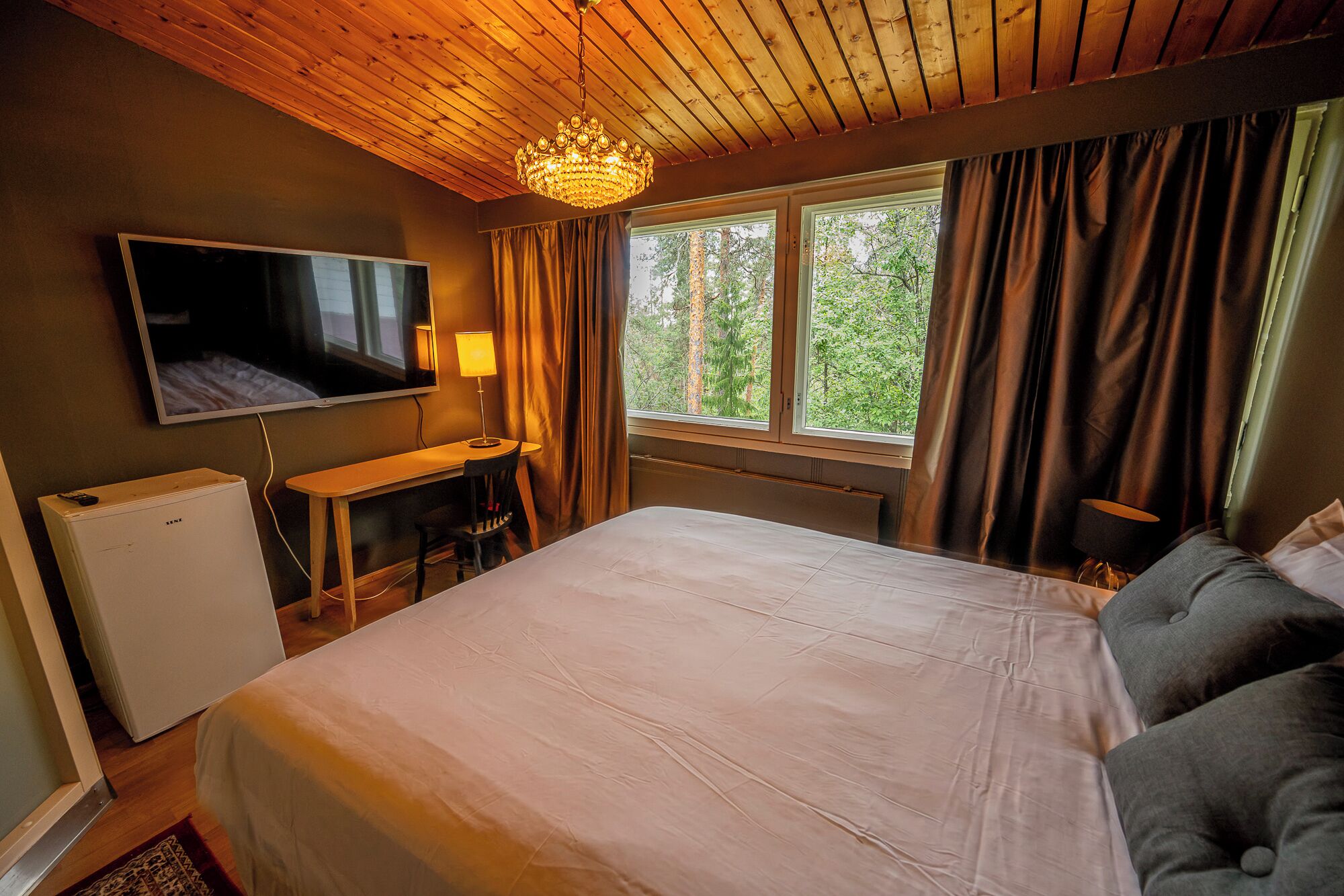 Une chambre à coucher avec un lit, un bureau, une télévision et une fenêtre avec des rideaux.