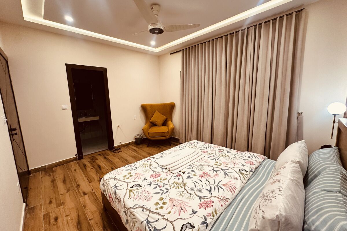 Un dormitorio con cama, una silla, ventilador de techo y ventana con cortinas.