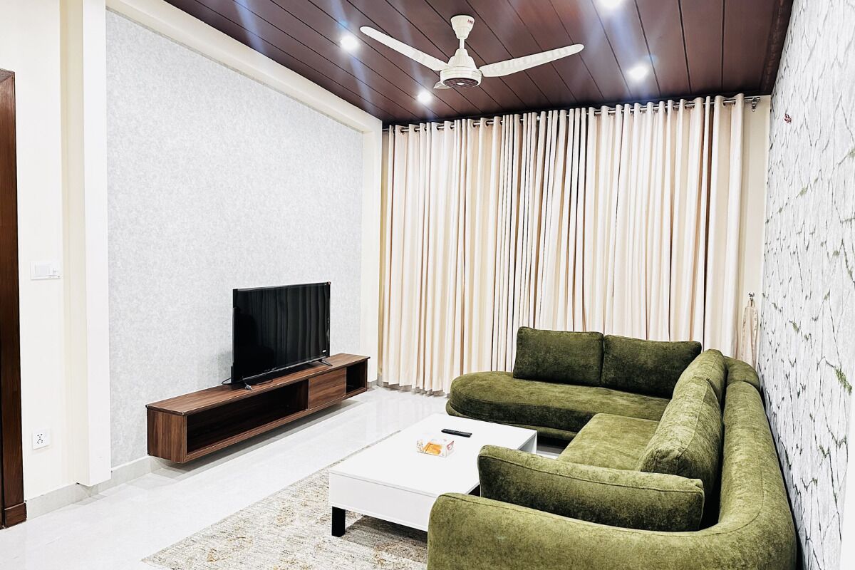 Una sala moderna con un televisor de pantalla plana, un sofá verde, una mesa de centro blanca y un ventilador de techo.