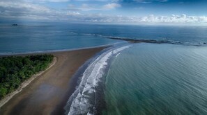 An aerial view of a beach with a clear sky, calm sea, and a sandy shore with vegetation. - Overhang Villa above ocean & Jungle-concierge (Bahía Ballena)
