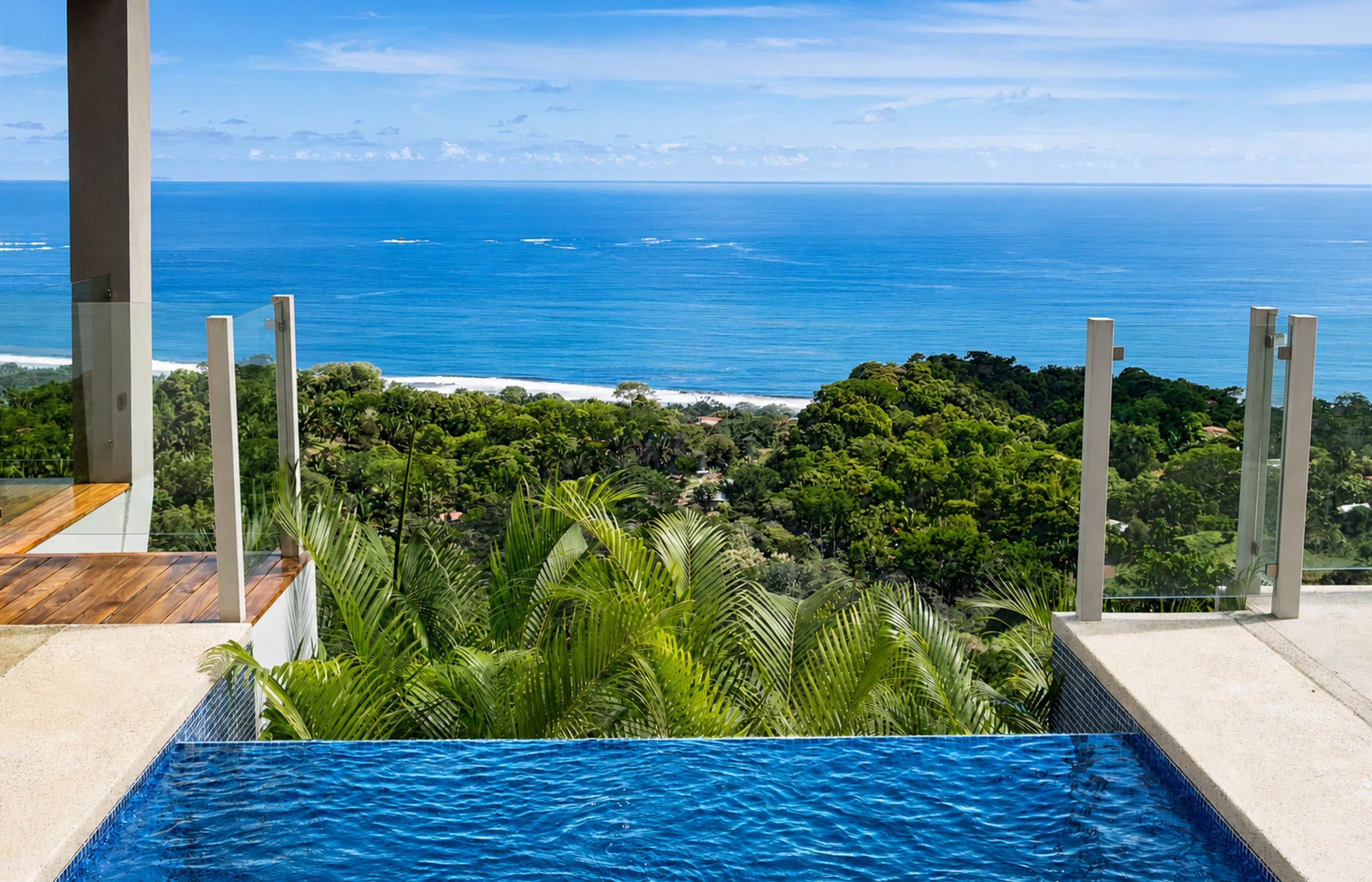 A modern outdoor pool with a view of the ocean and lush greenery.