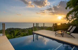 Une piscine à débordement offrant une vue sur l’océan et le coucher de soleil.