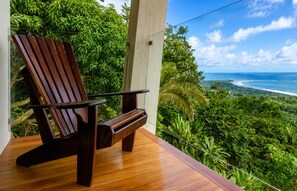 A wooden deck with a single chair overlooking a lush green landscape and a view of the ocean. - Overhang Villa – Oceanview & Infinity Pool | Uvita (Bahía Ballena)