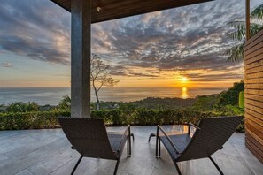 A terrace with two lounge chairs facing a sunset view over the ocean. - Luxury Oceanview Villa – Infinity Pool | Uvita (Bahía Ballena)