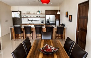 A modern kitchen with a central island, bar stools, and a dining table with chairs. - Luxury Oceanview Villa – Infinity Pool | Uvita (Bahía Ballena)