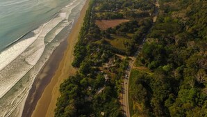 An aerial view of a coastal area with a beach, dense vegetation, and a road. - Luxury Designer villa Oceanview HR3 - Concierge (Bahía Ballena)