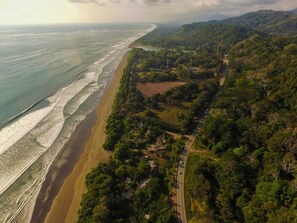 Luftaufnahme einer Küstenlandschaft mit Strand, dichter Vegetation und einer Straße.