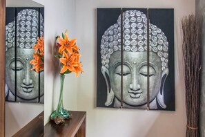 A wall with a large Buddha painting, a vase with orange flowers, and a bundle of sticks. - Luxury Oceanview Villa – Infinity Pool | Uvita (Bahía Ballena)
