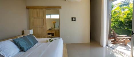 A hotel room with a bed, a wooden wardrobe, a small table with a vase, and a balcony with chairs.