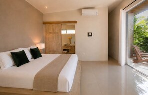A modern bedroom with a large bed, a wooden wardrobe, a small table with a vase, and a view of greenery through a glass door. - Luxury Oceanview Villa – Infinity Pool | Uvita (Bahía Ballena)