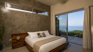 A modern bedroom with a large bed, a view of the outdoors, and a concrete wall. - Luxury Designer villa Oceanview HR3 - Concierge (Bahía Ballena)